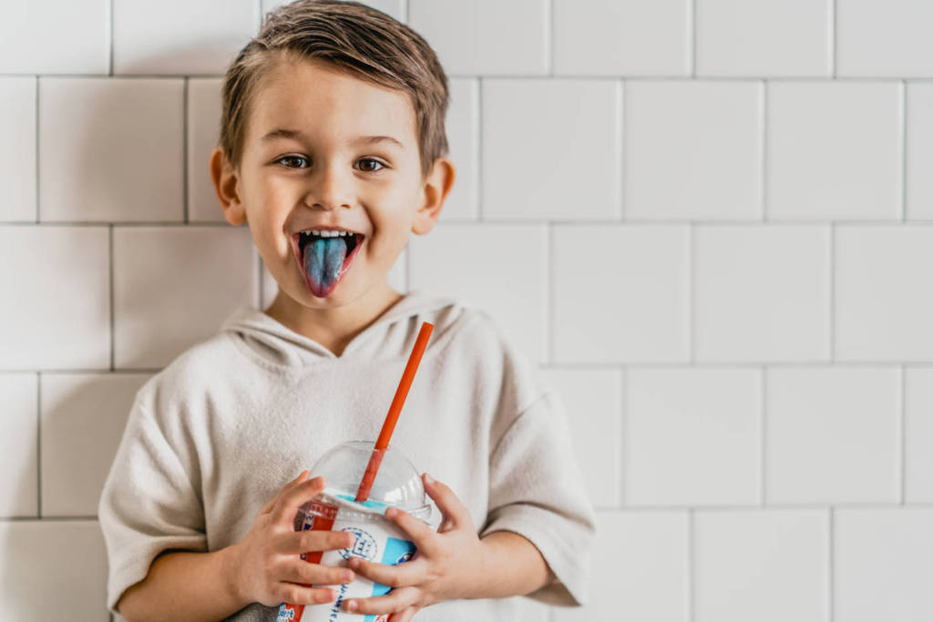 A boy drinking a blue ICEE sticking out his blue tongue