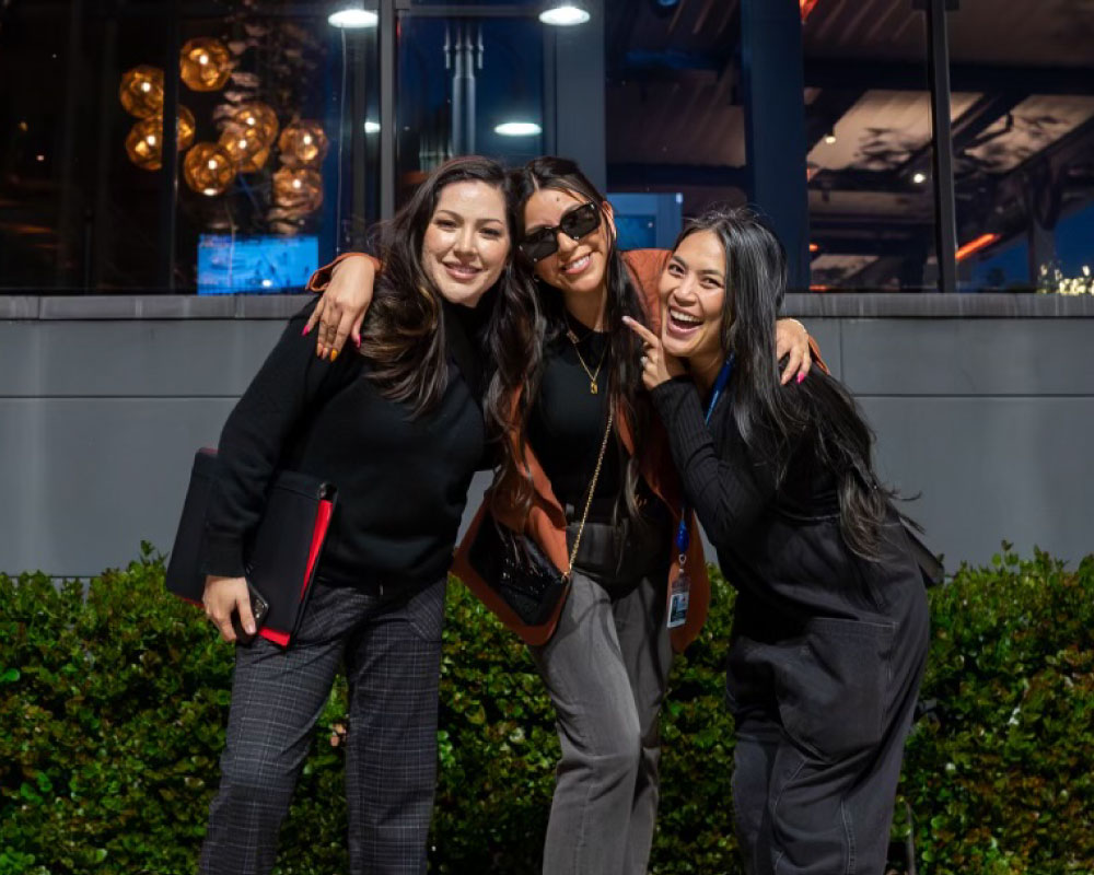 Joann Mercado Hicks (far right) posing with two smiling colleagues outside a nighttime venue.